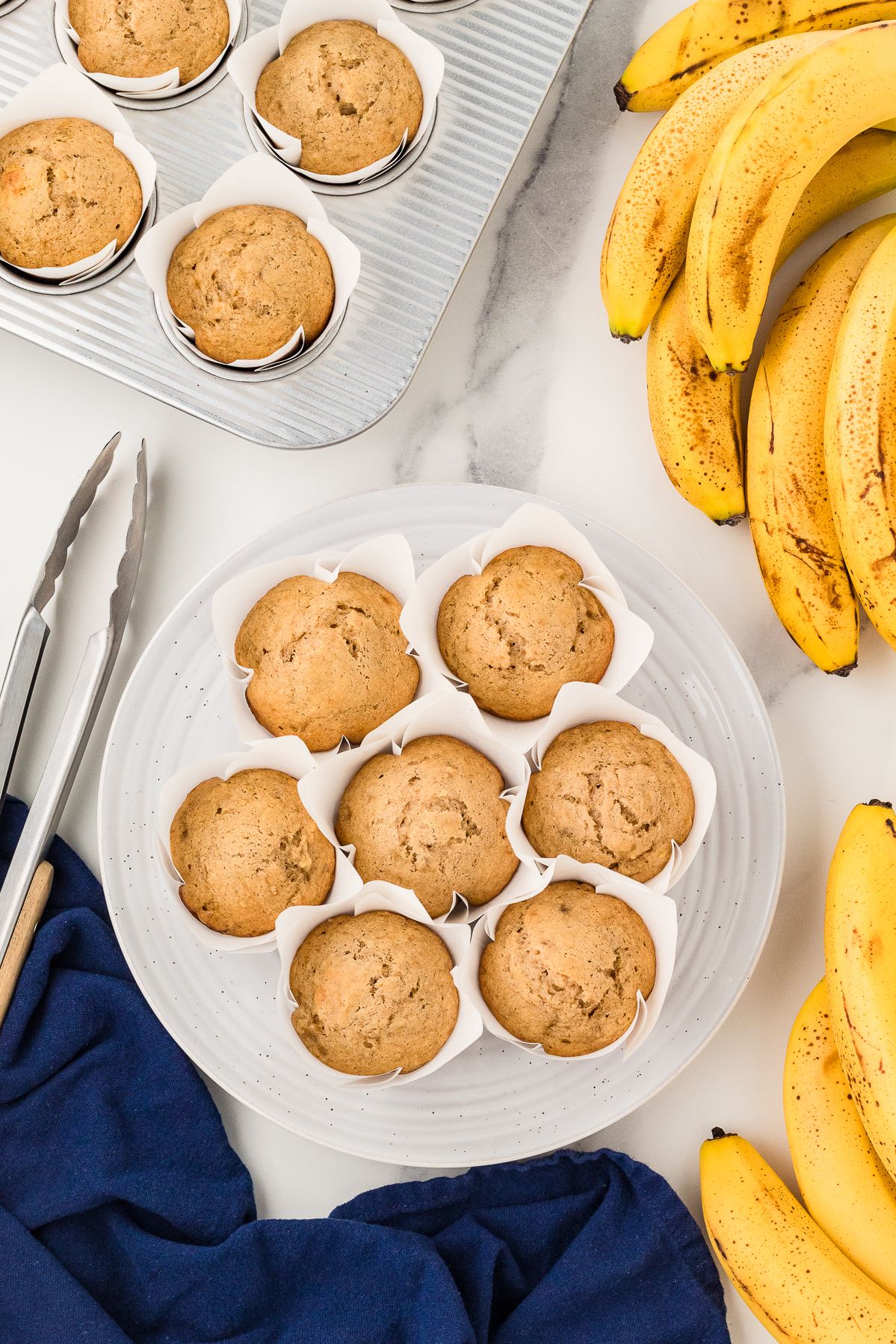 Overhead view of banana muffins on a plate with ripe bananas