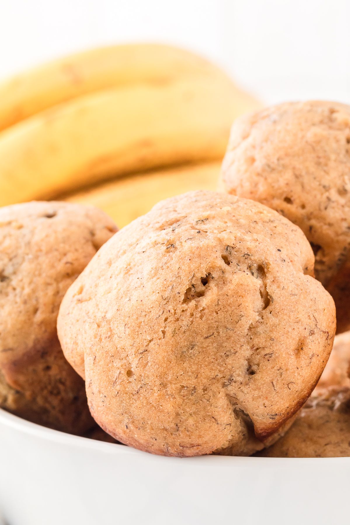 Healthy banana muffins in a white bowl with ripe bananas