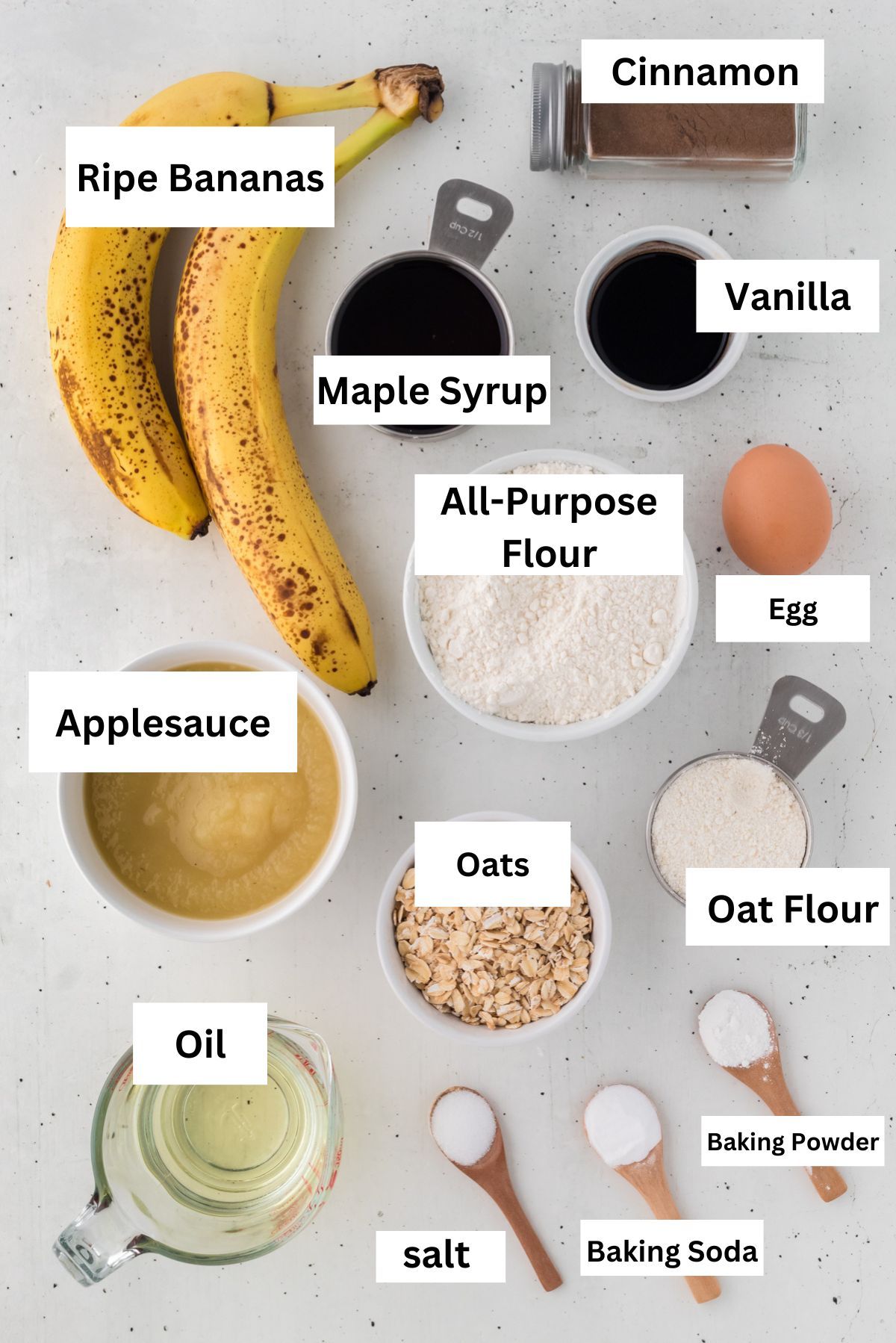Labeled ingredients for healthy banana muffins: ripe bananas, maple syrup, applesauce, oats, oat flour and cinnamon