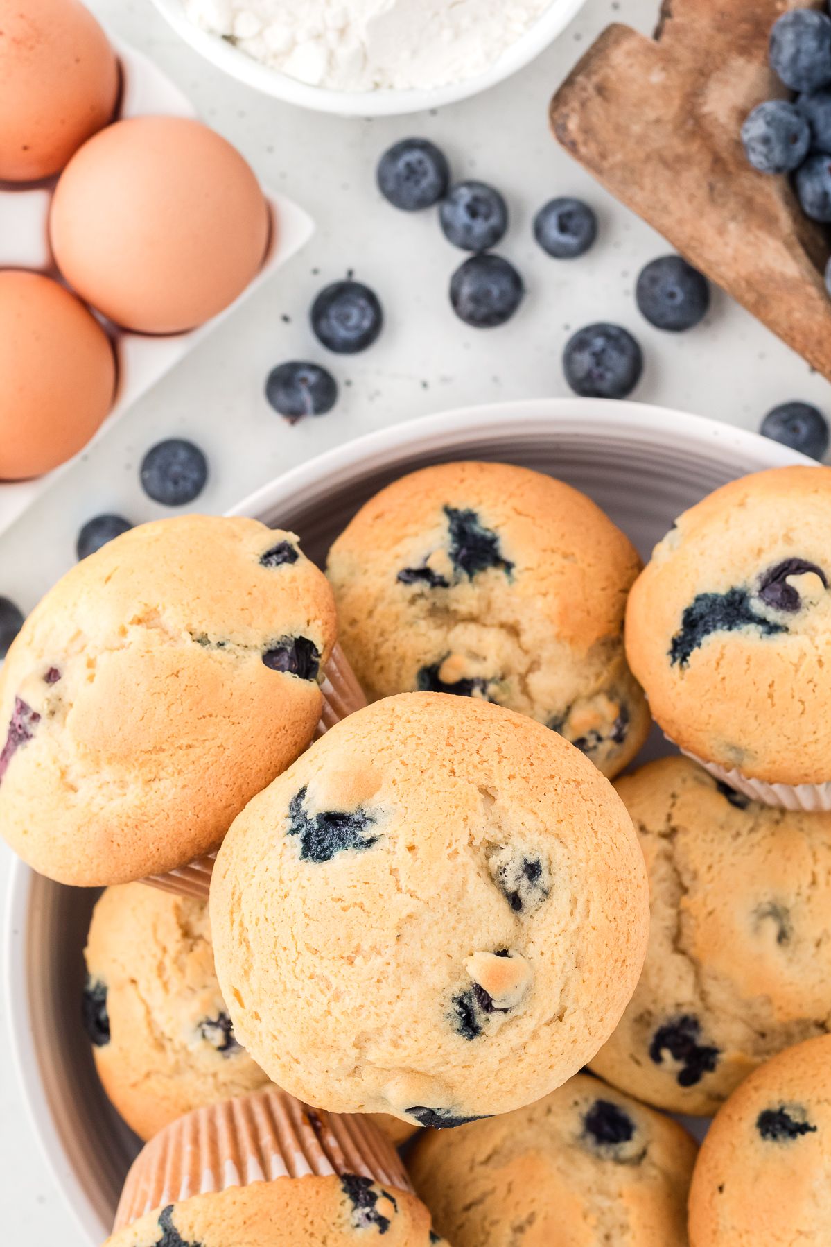 Healthy blueberry muffins piled in a bowl with fresh blueberries and eggs