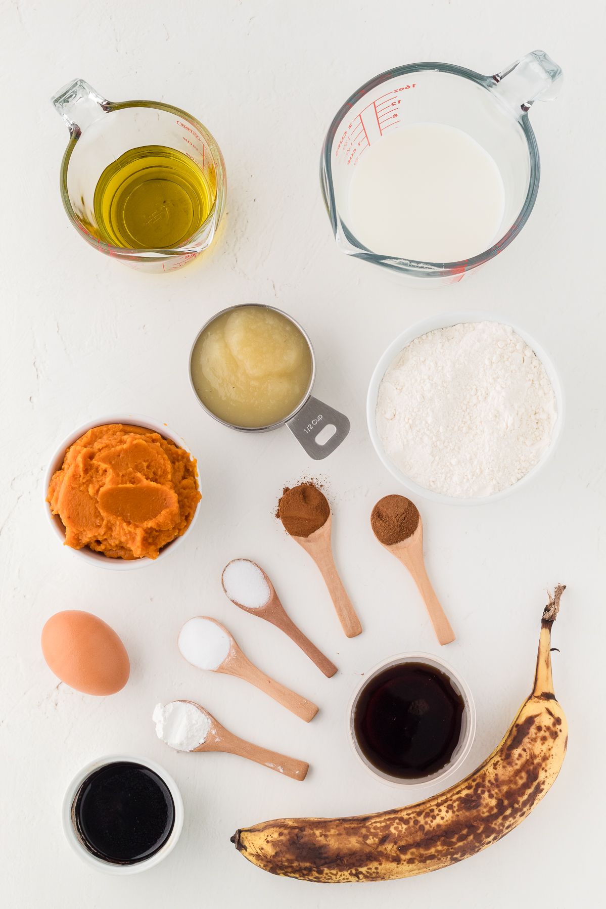 Ingredients for healthy pumpkin muffins including pumpkin puree, ripe banana, oil, maple syrup, flour and spices