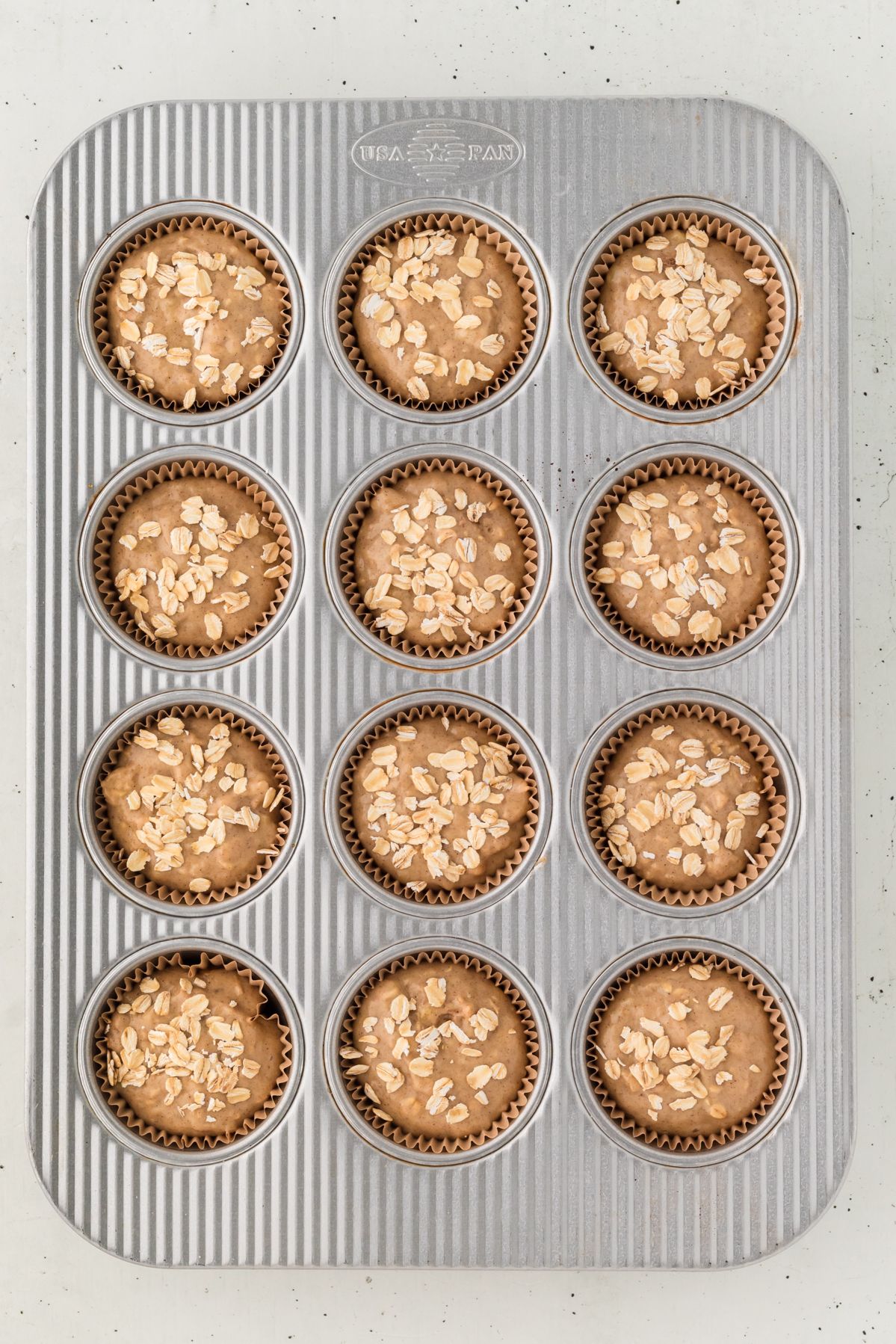 Banana oatmeal muffin batter topped with oats in a muffin tin