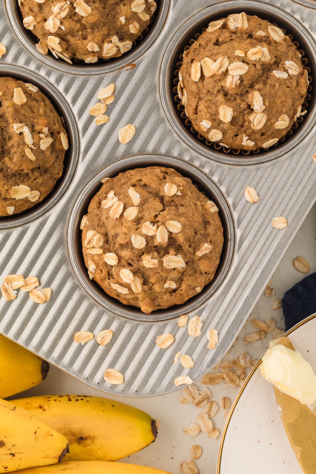 Oat topped banana oatmeal muffins in the pan with bananas