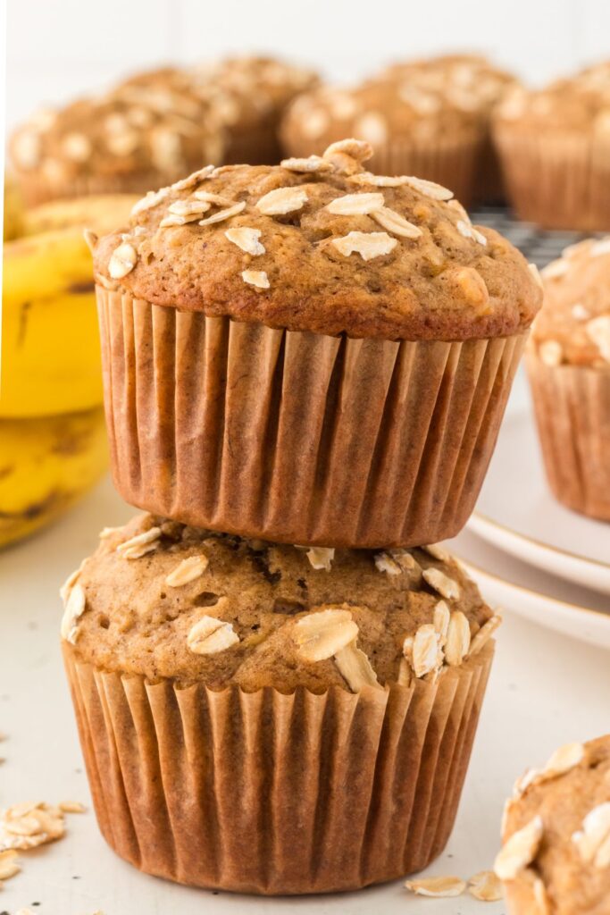 Two banana oatmeal muffins stacked with oats on top