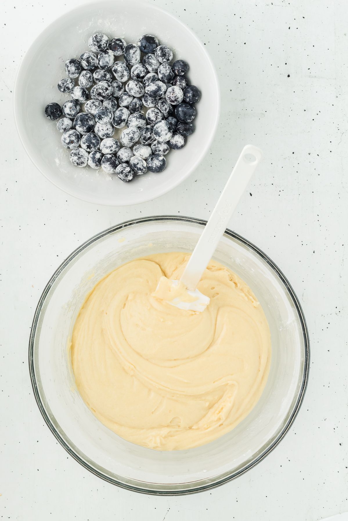 Blueberries tossed in flour next to lemon muffin batter