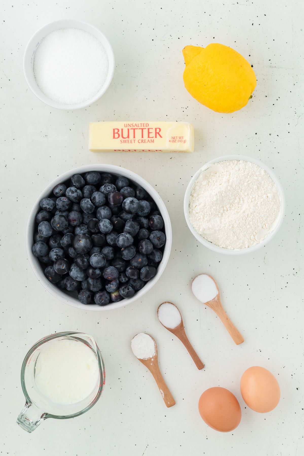 Ingredients for lemon blueberry muffins: fresh blueberries, lemon, butter, sugar, flour, milk and eggs