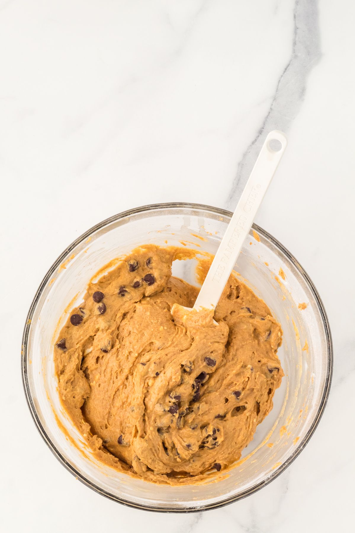 Pumpkin chocolate chip muffin batter in a glass mixing bowl with a spatula