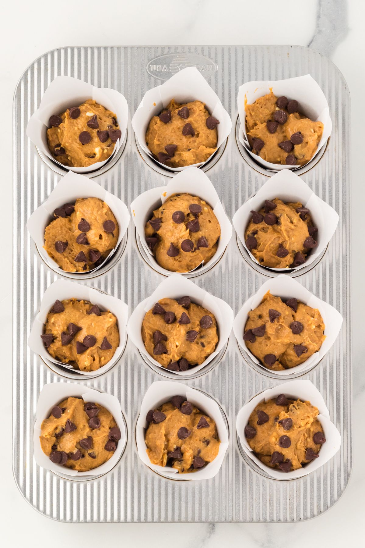 Pumpkin chocolate chip muffin batter scooped into a lined muffin tin